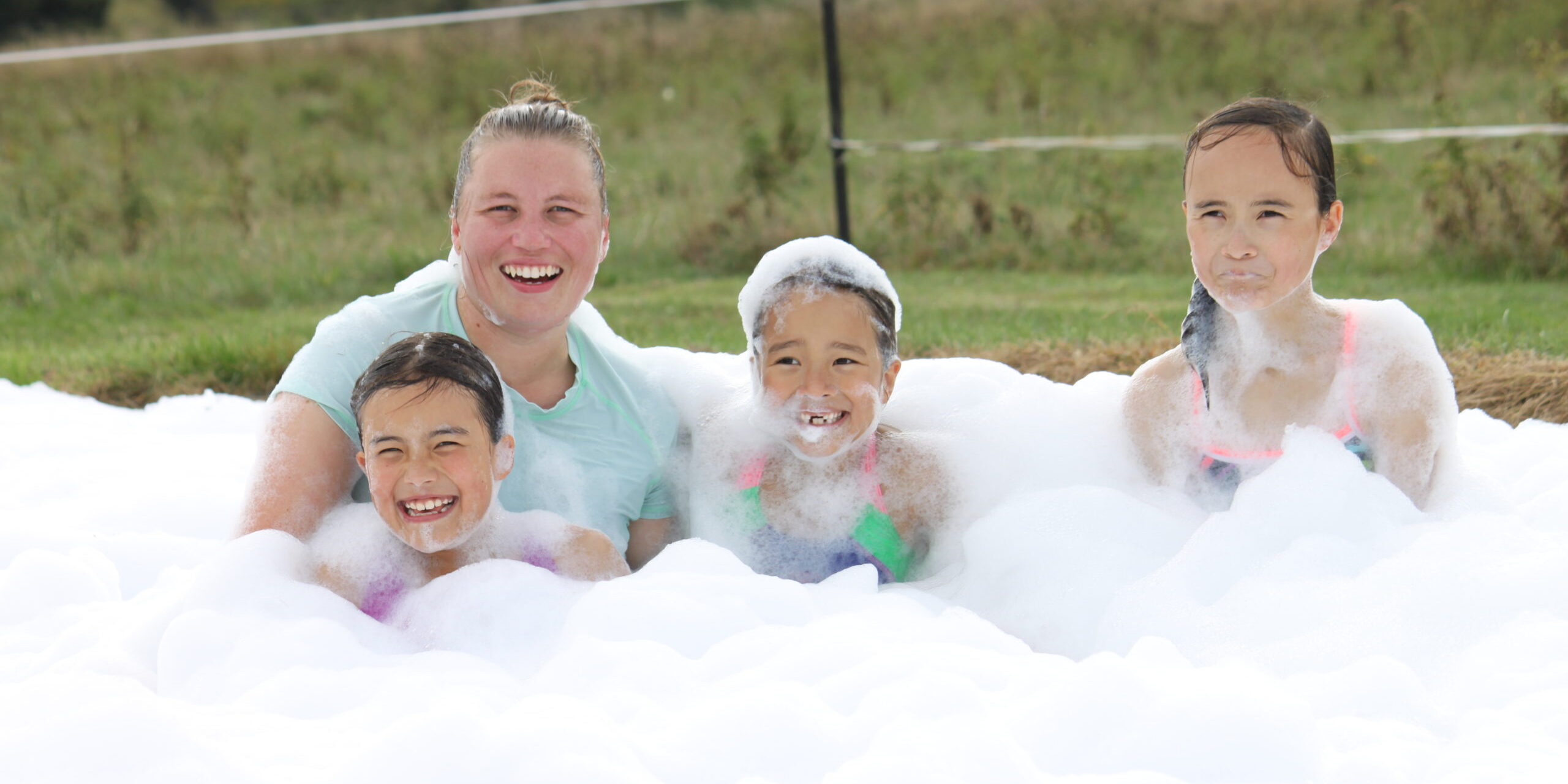 Four people sitting in a large pile of bubbles laughing